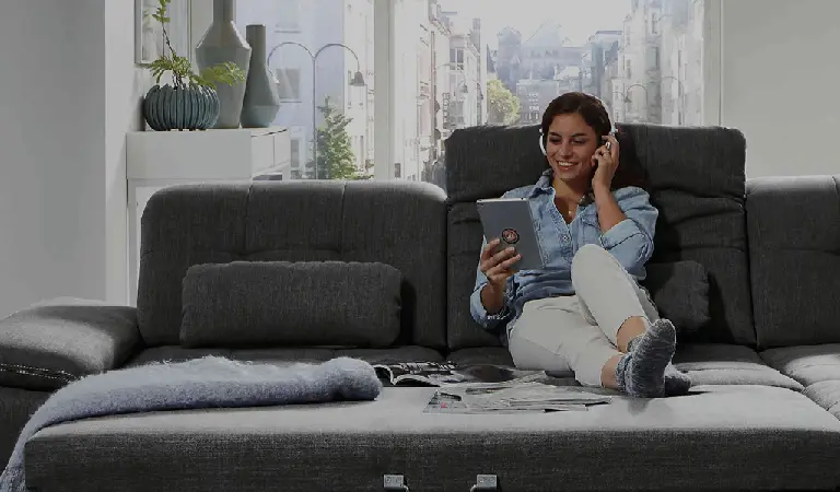 Frau sitzt entspannt auf grauem Sofa und liest die Möbelhaus Salzwedel Werbung mit günstigen Angeboten zu Sofas und Wohntrends. Moderner Wohnraum, gemütliche Atmosphäre und Fokus auf preiswerte Möbel Highlights.